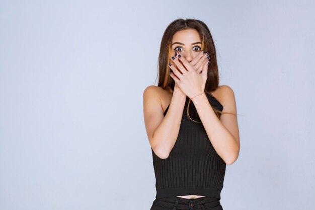 Femme en chemise noire couvrant son visage avec les mains.