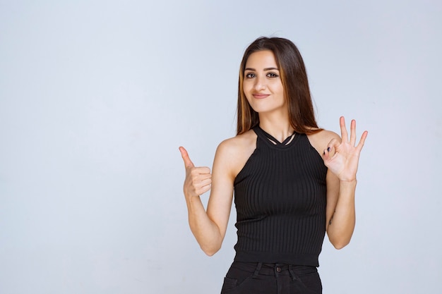 Femme en chemise noire faisant signe de la main positive.