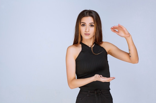 Femme en chemise noire montrant la mesure d'un objet.