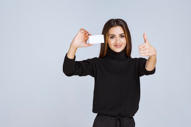 femme en chemise noire montrant sa carte de visite et semble satisfaite.