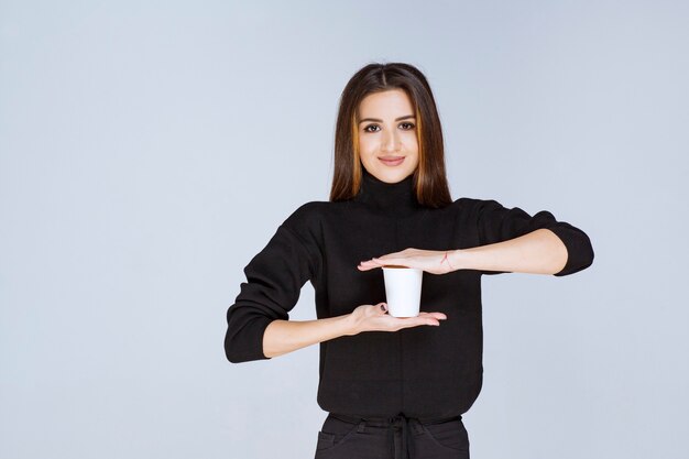 femme en chemise noire tenant une tasse de café jetable et en faisant la promotion.