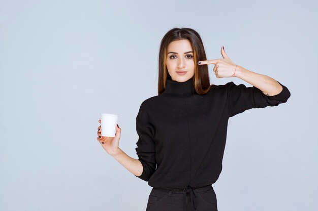 femme en chemise noire tenant une tasse de café et réfléchissant à de nouvelles idées.