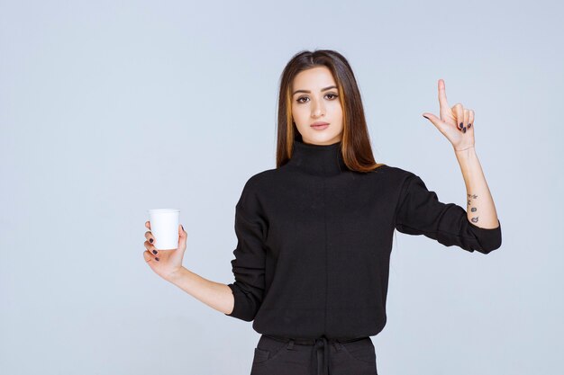 femme en chemise noire tenant une tasse de café et réfléchissant à de nouvelles idées.