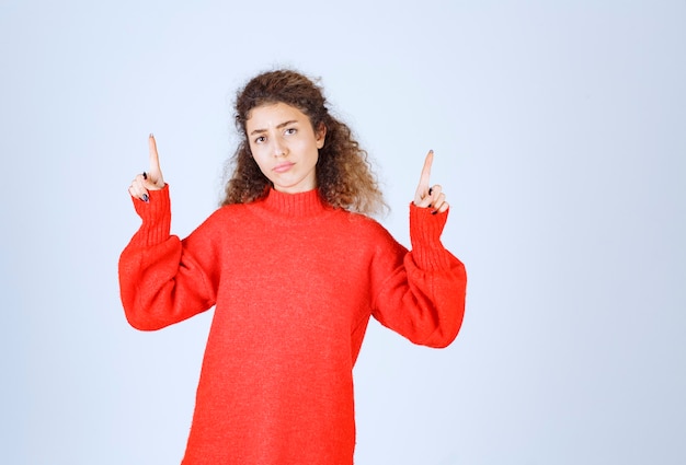 femme en chemise rouge pointant vers quelqu'un ou quelque part avec un visage émotionnel sur bleu.