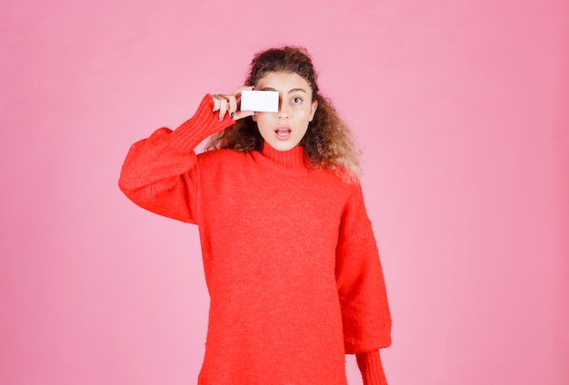 Photo gratuite femme en chemise rouge tenant une carte de visite à ses yeux.