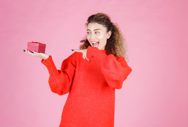 femme en chemise rouge tenant une petite boîte cadeau rouge.