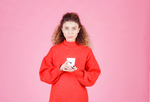 femme en chemise rouge tenant une tasse de café jetable.