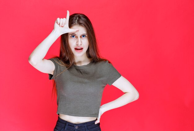 Femme en chemise verte montrant le signe de la main du perdant.