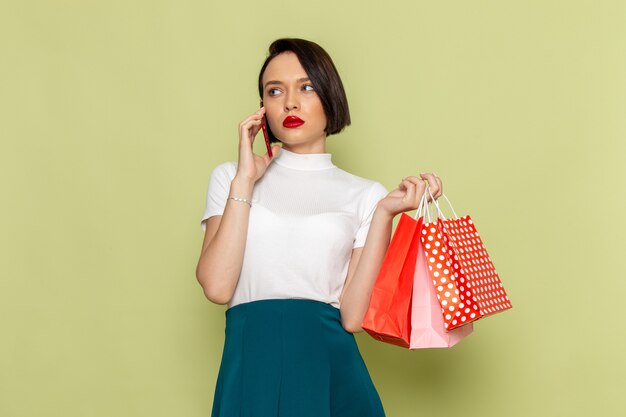 Femme en chemisier blanc et jupe verte tenant des colis et parler au téléphone