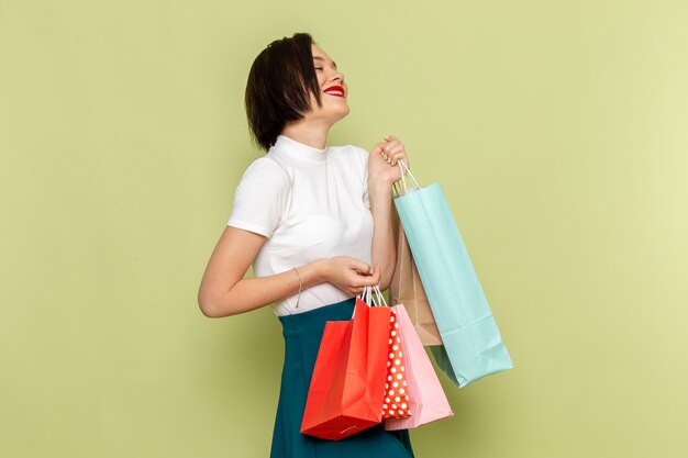 Femme en chemisier blanc et jupe verte tenant des paquets commerciaux avec sourire et pose mannequin de vêtements féminins