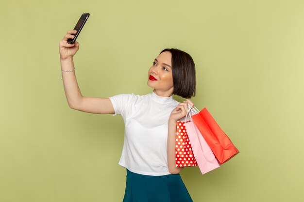 Femme en chemisier blanc et jupe verte tenant des paquets de shopping prenant un selfie