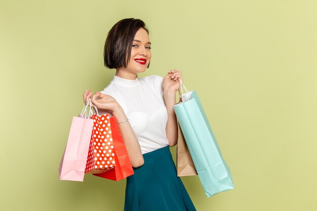 femme en chemisier blanc et jupe verte tenant des paquets shopping et souriant