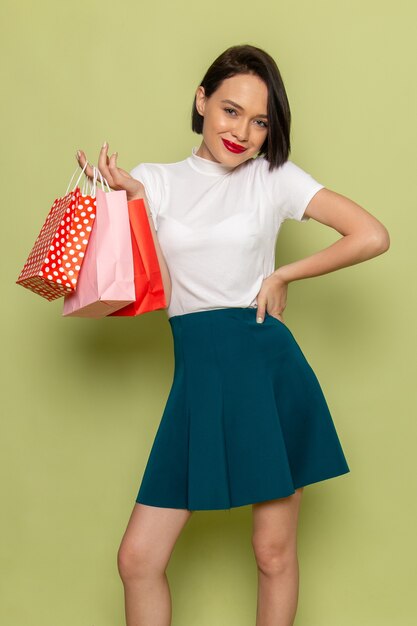 femme en chemisier blanc et jupe verte tenant des paquets shopping et souriant