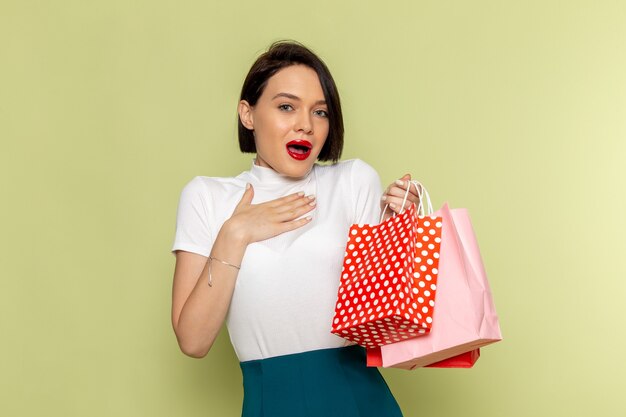 femme en chemisier blanc et jupe verte tenant des paquets shopping