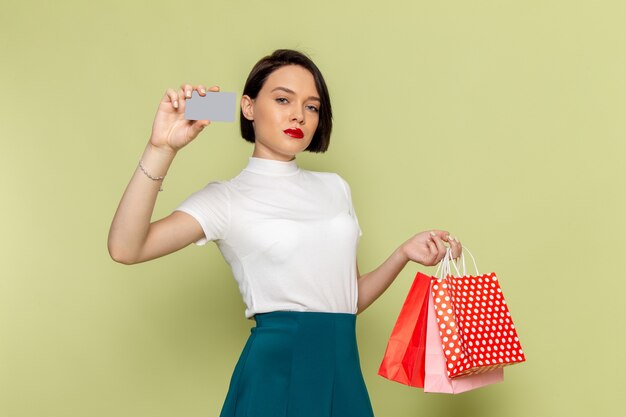 femme en chemisier blanc et jupe verte tenant des paquets shopping