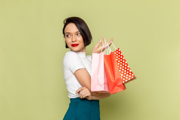 femme en chemisier blanc et jupe verte tenant des paquets shopping