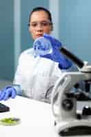 Photo gratuite femme chercheuse biochimiste tenant une boîte de pétri analysant une solution bleue travaillant à une expérience scientifique dans le laboratoire de l'hôpital de biochimie. médecin scientifique biologiste examinant un échantillon de micro-organisme