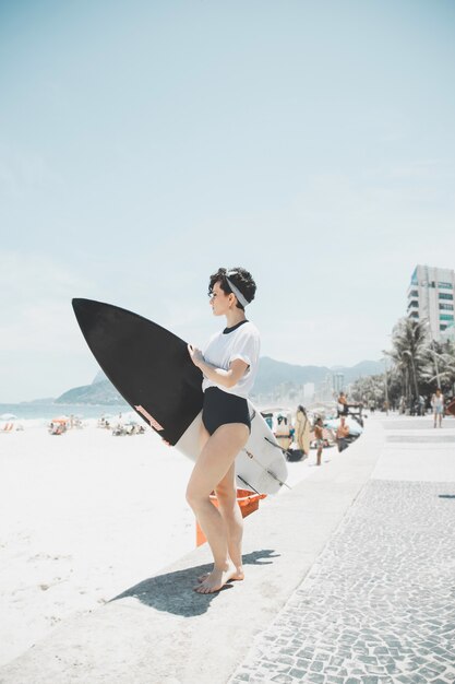 Femme cheveux bouclés tenant une planche de surf sur la plage de Rio de Janeiro