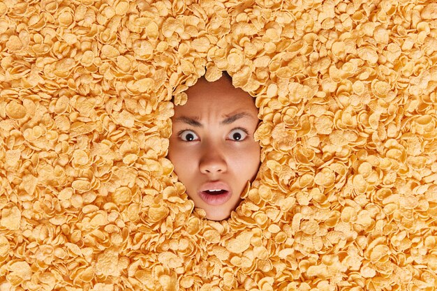 Une femme choquée et embarrassée regarde avec une expression indignée noyée dans des cornflakes secs avec une nutrition et une ration alimentaire équilibrées