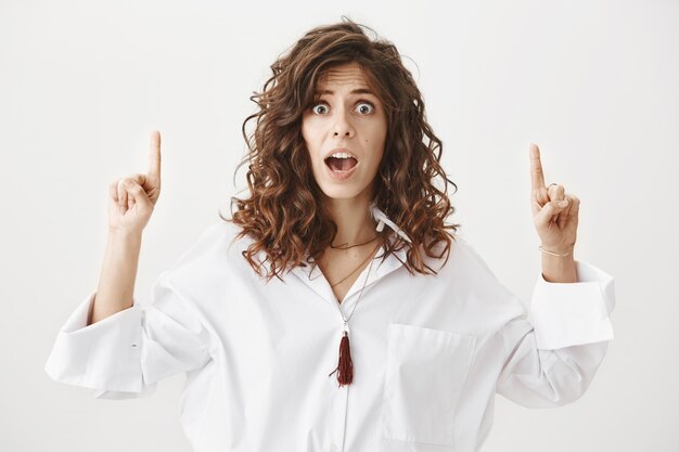 Femme choquée et inquiète pointant les doigts vers le haut