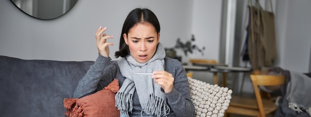 Photo gratuite une femme choquée semble inquiète de voir son thermomètre attraper un rhume et avoir de la fièvre, assise en congé de maladie à