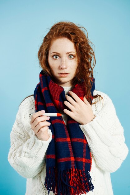 Femme choquée avec thermomètre numérique vérifiant la température au studio shot