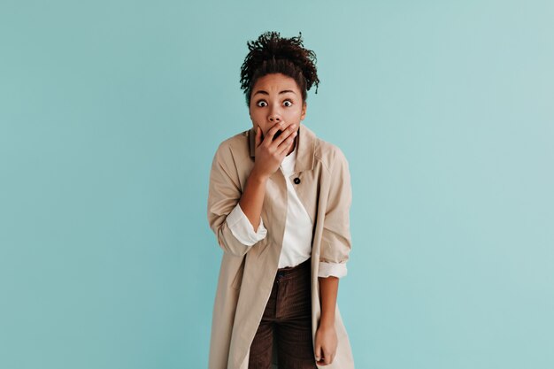 Femme choquée en trench-coat couvrant la bouche avec la main