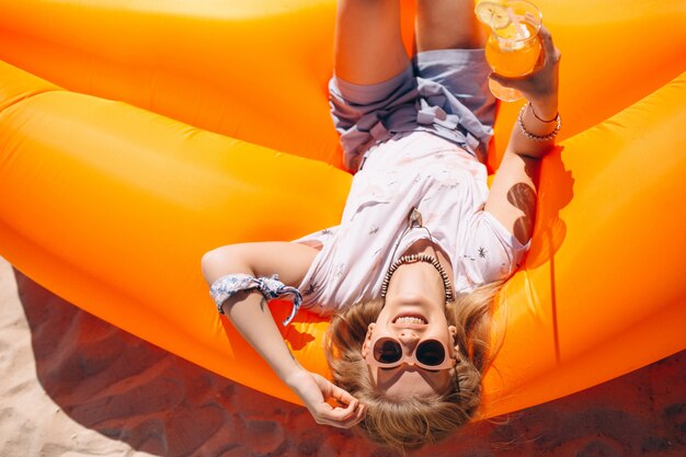 Femme avec coctail allongé sur un matelas de piscine à la plage