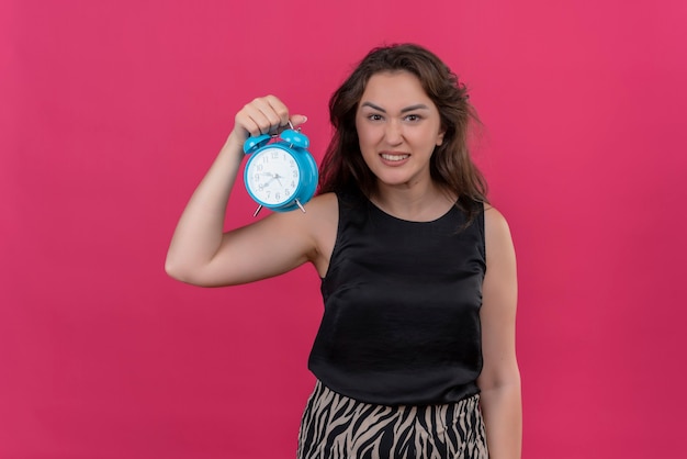 Femme en colère portant maillot noir tenant un réveil sur mur rose