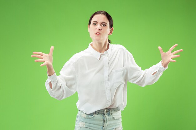 Femme en colère regardant la caméra. Femme d'affaires agressive debout isolée sur fond de studio vert branché. Portrait de femme demi-longueur.