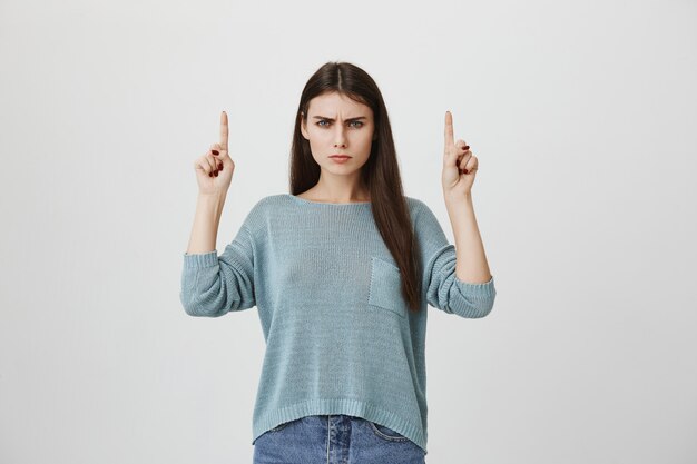 Photo gratuite femme en colère sceptique pointant les doigts vers le haut, plissant les yeux bouleversé