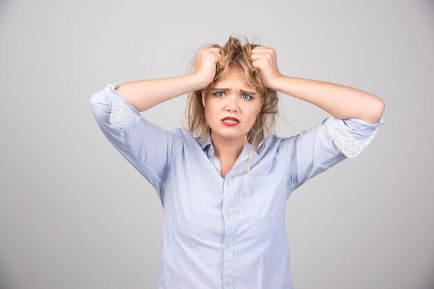 Femme en colère tirant ses cheveux sur une surface grise