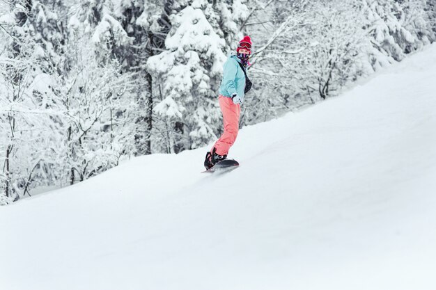 Femme en combinaison de ski regarde par-dessus son épaule en descendant la colline sur son snowboard