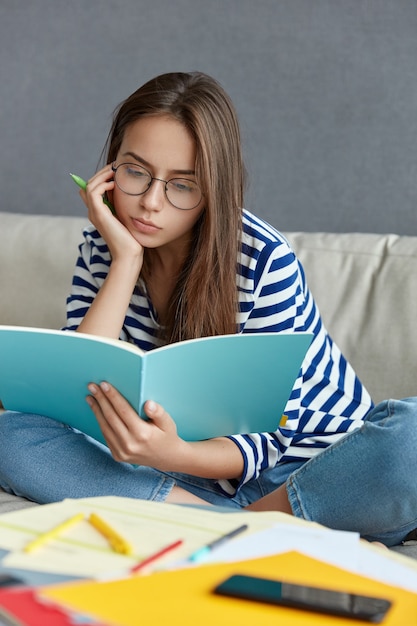 Femme concentrée dans des lunettes optiques, réfléchit à des idées créatives pour la publication, tient un stylo