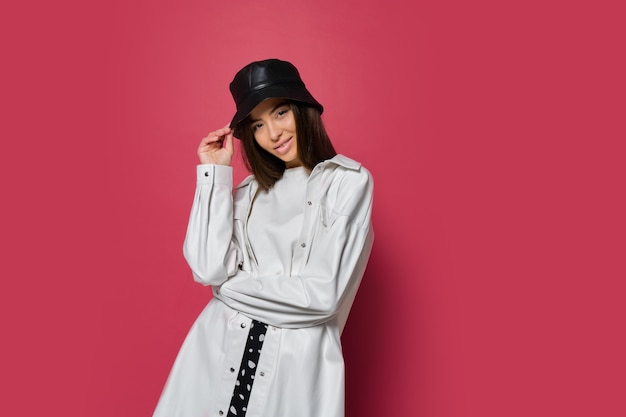 Femme confiante avec un sourire parfait habillé en casquette élégante et veste blanche posant sur fond rose. Isoler.