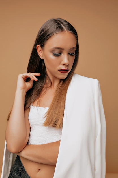 Femme confiante en vêtements blancs avec maquillage lumineux regardant vers le bas. Photo de Studio de femme élégante