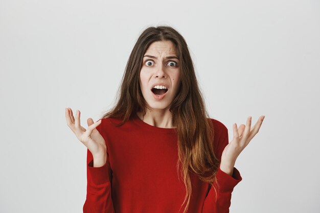 Une femme confuse et frustrée lève les mains avec consternation, laisse tomber la mâchoire en embuscade