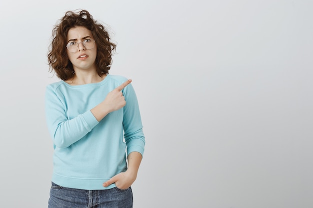 Femme confuse montrant quelque chose de bizarre, pointant le doigt à droite et à la douteuse