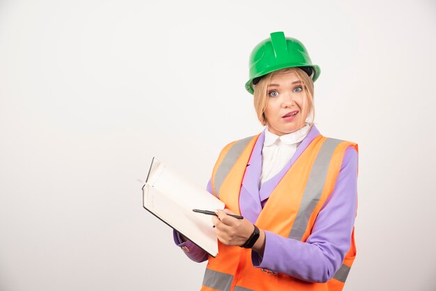 Femme constructeur en casque avec tablette sur mur blanc.