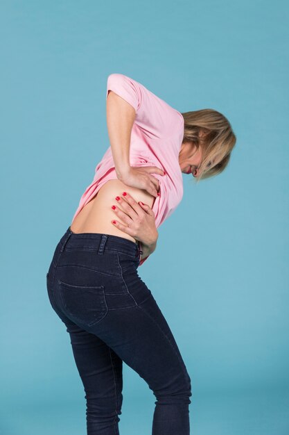 Femme contrariée souffrant de douleurs lombaires sur fond bleu