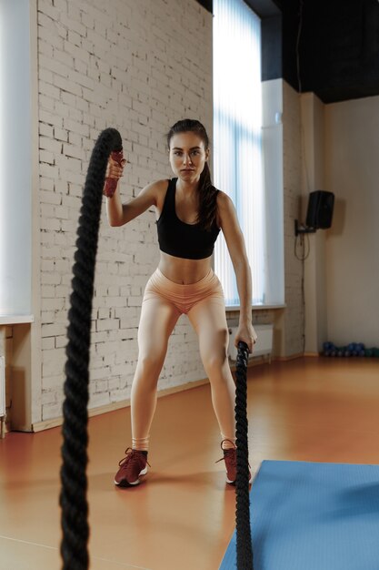 Femme avec des cordes de combat exercice dans la salle de fitness. Athlète, sport, corde, entraînement, entraînement, exercices et concept de mode de vie sain