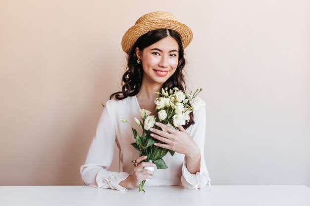 Femme coréenne extatique souriant tout en posant avec des fleurs. Blithesome femme asiatique bouclée tenant des eustomas blancs.