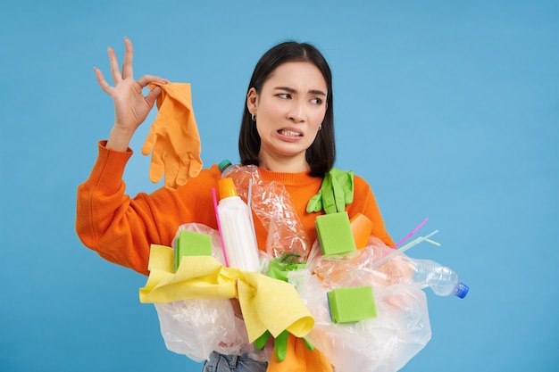 Photo gratuite une femme coréenne regarde un gant en latex puant détient des ordures en plastique nettoie la maison et recycle le backgro bleu