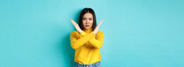 Photo gratuite femme coréenne sérieuse et affirmée montrant un geste d'arrêt croisé en fronçant les sourcils et en disant qu'il n'est pas interdit d'agir