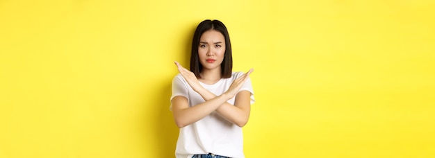 Photo gratuite femme coréenne sérieuse et affirmée montrant un geste d'arrêt croisé en fronçant les sourcils et en disant qu'il n'est pas interdit d'agir