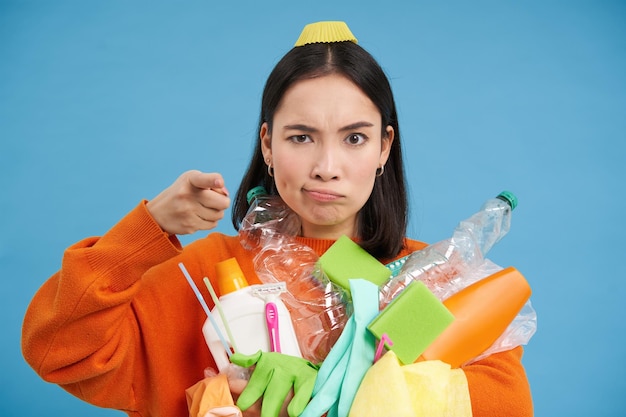 Photo gratuite une femme coréenne sérieuse pointant du doigt la caméra blâme les gens pour la pollution des ordures tenant du plast vide