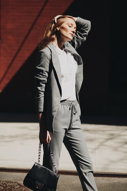 Femme en costume gris pose avec un sac noir dans la rue de New York