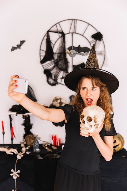 Femme en costume de sorcière faisant selfie avec le crâne