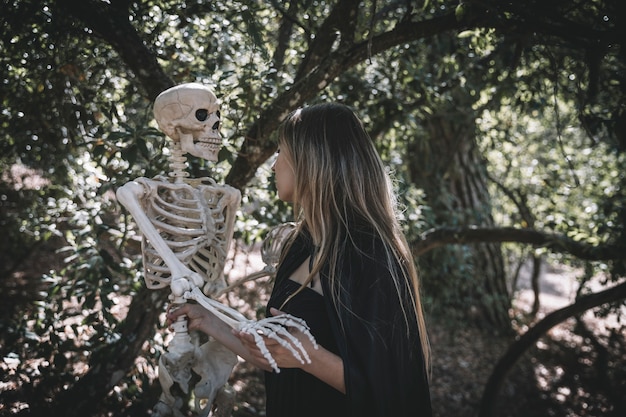 Femme en costume de sorcière tenant un squelette effrayant