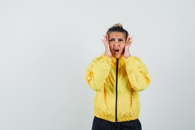 Femme en costume de sport, main dans la main sur les joues et à la triste, vue de face.